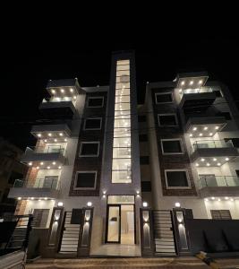 un edificio alto con luces encendidas por la noche en شقة مفروشة بغرفتي نوم الجاردنز en Umm Uthainah