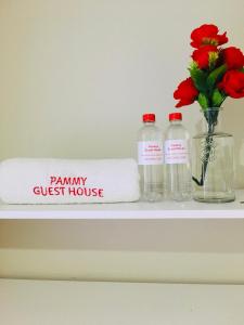 een plank met twee flessen en een handdoek en een vaas met bloemen bij Pammy Guest House in Richards Bay