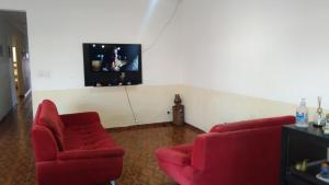 sala de estar con 2 sillas rojas y TV en pousada&Hostel perola mar en Mongaguá