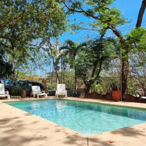 Casa Pura Vida Surf Hostel - Tamarindo Costa Rica في تاماريندو: مسبح فيه كراسي واشجار في ساحة