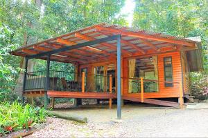 a wooden cabin with a large deck in the woods at Figtree Getaway in Malanda