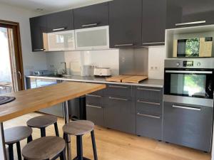 una cucina con armadi grigi, tavolo e sgabelli in legno di Le Shala - 55m² + Jardin a Tabanac Altre 6 foto
