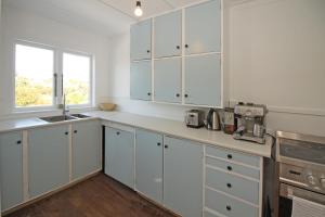 a white kitchen with white cabinets and a sink at Classic bach near the beach in Oneroa