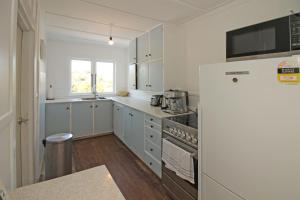 a kitchen with white cabinets and a refrigerator at Classic bach near the beach in Oneroa +23 photos