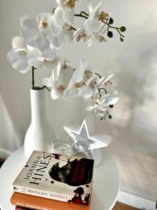 a table with a book and a vase with white flowers at Batalionów Apartment in Warszawa
