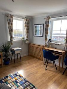 a living room with a desk and two windows at Da Peerie Hoose in Hamnavoe