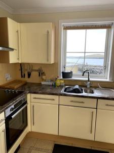 a kitchen with white cabinets and a sink and a window at Da Peerie Hoose in Hamnavoe