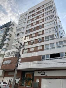 un edificio blanco alto con una tienda delante en Apartamento a 100m da beira-mar en Capão da Canoa