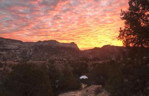 um pôr-do-sol num desfiladeiro com árvores e montanhas em Escalante Yurts - Luxury Lodging em Escalante