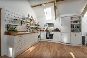 a large kitchen with white cabinets and wooden floors at Gilliflower 1 bedroom cottage at Trethwale Barns Holiday Home in Saint Keyne