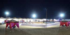 ジャイサルメールにあるRomiyo Desert Campの夜間のビーチでの椅子とパラソルのグループ