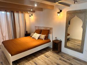 - une chambre dotée d'un lit avec des draps orange et un miroir dans l'établissement Maison provençale au bord de l’eau, à Istres