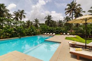 ベノーリムにあるSilva Heritage Resort Goaのスイミングプール(椅子、パラソル付)