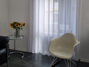 a white chair sitting next to a window with a vase of flowers at Am Basler Tor in Grenzach-Wyhlen
