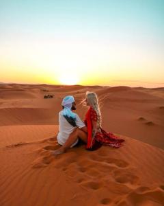 梅爾祖卡的住宿－Desert Sparrow Luxury Camp，坐在沙漠中的男人和女人,看着日落