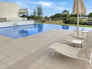 uma piscina com duas cadeiras brancas e um guarda-sol em Kirra Penthouse with Private Spa em Gold Coast