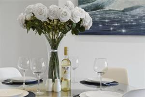 a table with a bottle of wine and a vase of white roses at Ahoy There! in Hythe