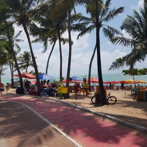 een strand met palmbomen en tafels en parasols bij Excelente quarto/sala in Maceió