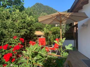 un patio con sombrilla, sillas y flores rojas en Ferienhaus Haas, en Ruhpolding