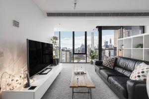 een woonkamer met een zwarte leren bank en een tv bij Cradle the Clouds - Southbank Stay with Parking in Melbourne