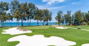 a golf course with palm trees and the ocean at Bonneville Beach House in Thai Muang