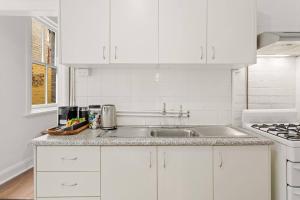 Una cocina con gabinetes blancos y un fregadero. en Harbourfront meets Heritage Chic near Barangaroo, en Sídney