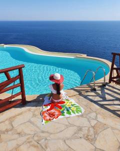 une femme assise sur une chaise à côté d'une piscine dans l'établissement Vista mozzafiato a picco sul mare Villa Patty, à Torre delle Stelle