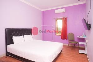 a bedroom with a white bed and a purple wall at Janna Guest House SYARIAH Yogyakarta Mitra RedDoorz in Yogyakarta