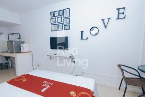a white room with a bed and a tv on the wall at Redliving Apartemen Grand Sentraland - AT Properti Tower Pink in Karawang