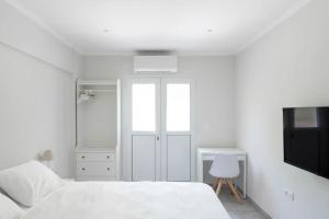 een witte slaapkamer met een bed en een televisie bij Voula's Secret Garden Studio in Athene