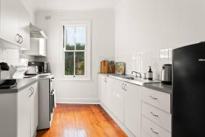 een keuken met witte kasten en een zwarte koelkast bij Contemporary Charm with Spectacular Harbour Views in Sydney
