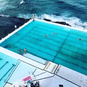 a swimming pool by the ocean with people in it at Bondi Oasis: 2BR + Balcony Bondi Beach in Sydney