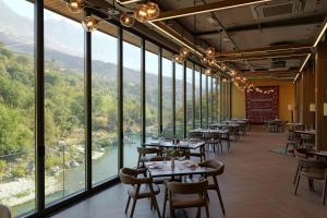 a restaurant with tables and chairs and large windows at Hotel Uji Ftohte Tepelene in Tepelenë