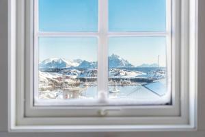 a window with a view of a marina and snow covered mountains at Huset i Stamsund in Rishaugen