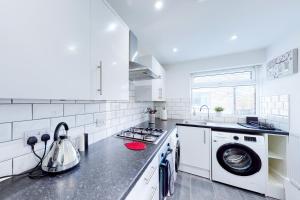eine weiße Küche mit einer Waschmaschine und einem Waschbecken in der Unterkunft Stunning Ranworth House Sleeps 5 in Bedford