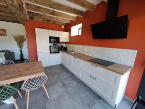 una cucina con pareti arancioni, armadi bianchi e tavolo di Gîte du Plantagenêt - Piscine intérieure privative a Rouez