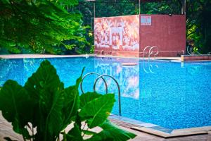 a swimming pool with blue water and green plants at Srushti Farms Resort in Vasind