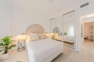 a white bedroom with a white bed and a mirror at Alojarte Bécquer recien reformado Free parking in Seville