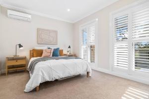 a white bedroom with a bed and two windows at Spacious Luxury Hampton Home - Park Front in Melbourne