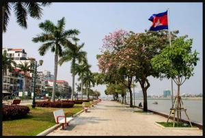 a sidewalk with benches and a flag flying over a river at Hotel De Palace in Phnom Penh