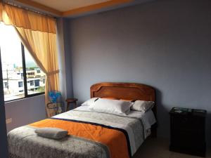 um quarto com uma cama com um cobertor laranja e uma janela em Centro Macas em Macas