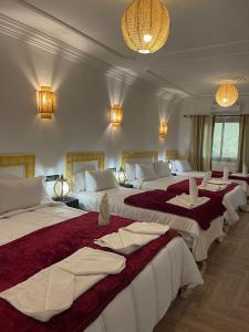 a hotel room with three beds with red and white sheets at Hôtel Bia Besta in Boumalne