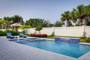 - une piscine avec 2 chaises et un parasol dans l'établissement Luxe Palm Beach Gardens Home with Private Pool and Spa, à Palm Beach Gardens