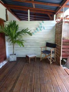 une terrasse en bois avec une chaise et un palmier dans l'établissement Bungalow atypique Ti Bambou à 500m de la plage, à Sainte-Anne