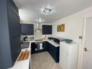 a kitchen with blue cabinets and a white refrigerator at Riverside 2 Bedroom Townhouse with Car Charger in Abergavenny