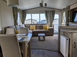 uma sala de estar com um sofá e uma mesa em Beautiful Pet Friendly Southerness Caravan With Sea View & Decking Area em Mainsriddle