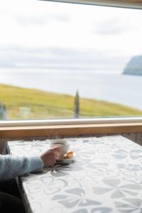 a person sitting on a train with a cup of coffee at Cottage with stunning view of the sea and islands. in Leynar