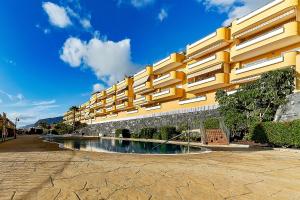 a large yellow building with a pool in front of it at Ocean view Family Apartment in Playa La Arena in Puerto de Santiago
