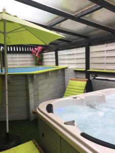 un patio con bañera de hidromasaje y sombrilla verde en Le Domaine de Charline de 1 à 35 personnes, en Issel