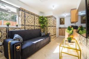 a living room with a black couch and a kitchen at Lux Versace Pad Sleeps 10 Hot Tub, Cinema & Games Room in London